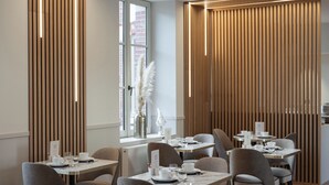 A modern dining area with wooden paneling, tables set with white tableware, and a view of the city through large windows. - Hôtel Margaux  (Epernay)