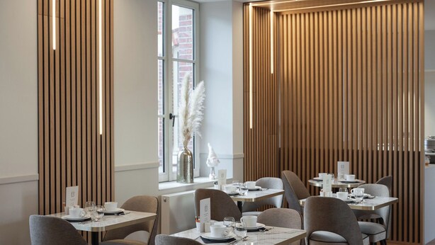 A modern dining area with wooden paneling, tables set with white tableware, and a view of the city through large windows. - Hôtel Margaux  (Epernay)