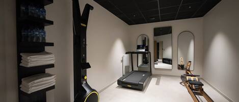 A gym with a treadmill, rowing machine, and shelves with towels.