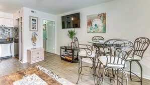 A modern kitchen with a built-in refrigerator, a dining area with metal chairs and a glass table, and a living space with a ceiling fan and artwork on the walls. - Hilton Head Island Condo w/ Coligny Beach Access! (Hilton Head Island)