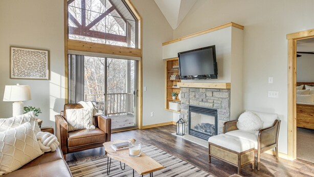 A spacious living room with a fireplace, leather sofas, a wooden coffee table, and a large TV mounted above the fireplace. - Nisswa Townhome w/ Boat Slip + Gull Lake Access! (Nisswa)
