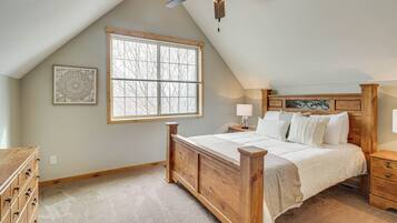 A bedroom with a sloped ceiling, a large window, a wooden bed, a nightstand, a dresser, and a ceiling fan.