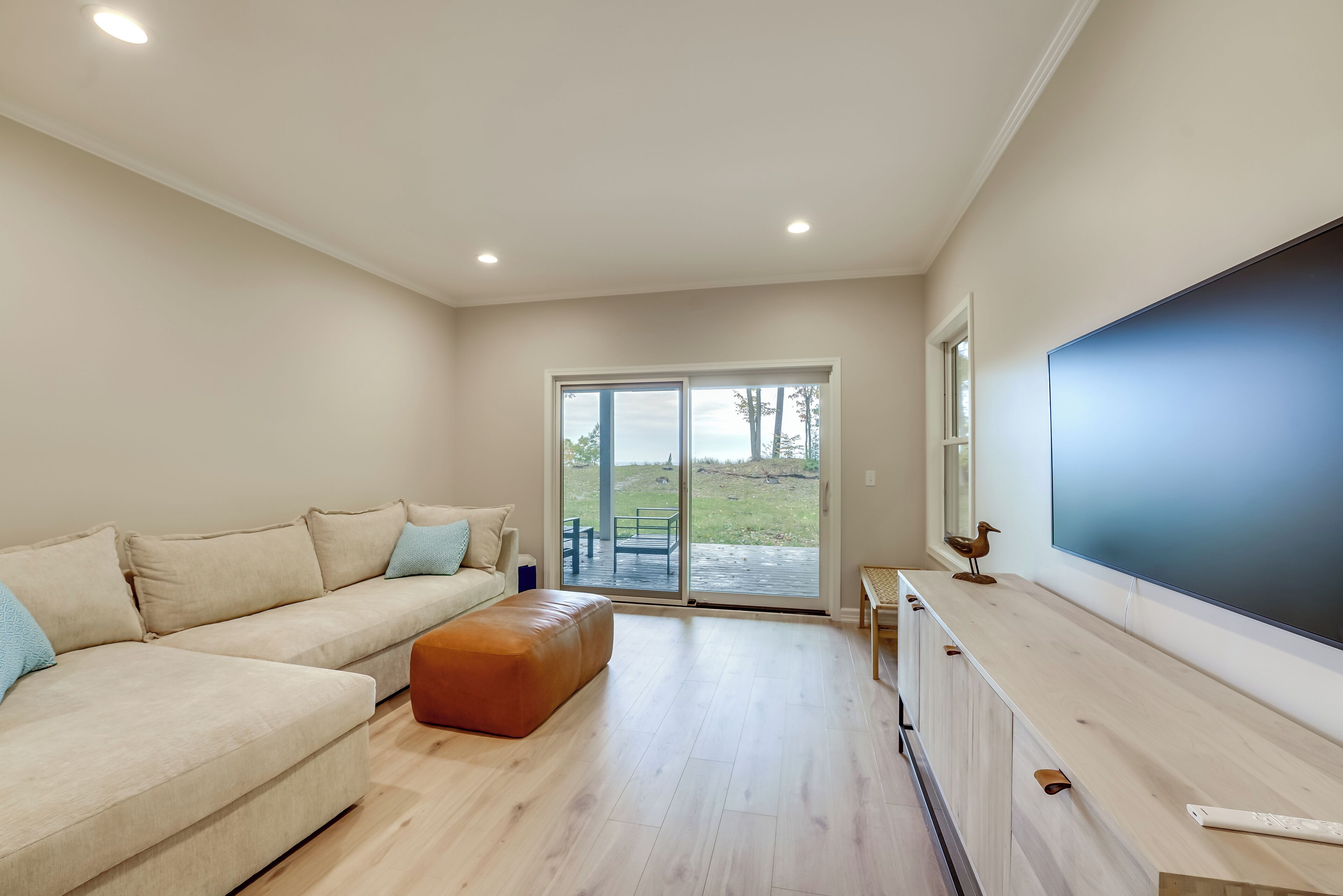 Una sala de estar moderna con un sofá seccional beige, una mesa de centro de madera y un televisor de pantalla plana grande sobre un mueble de madera.