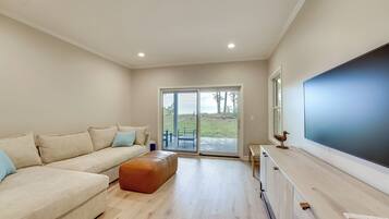 Una sala de estar moderna con un sofá seccional beige, una mesa de centro de madera y un televisor de pantalla plana grande sobre un mueble de madera.