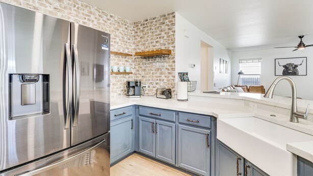 A modern kitchen with a stainless steel refrigerator, blue cabinets, and a brick accent wall. - Centrally Located Austin Home w/ Private Patio! (Austin)