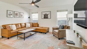 A modern living room with a sectional sofa, a coffee table, and a TV mounted on the wall. - Centrally Located Austin Home w/ Private Patio! (Austin)