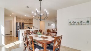 A dining area with a wooden table and chairs, a chandelier, and a kitchen in the background. - Centrally Located Austin Home w/ Private Patio! (Austin)