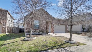 A residential house with a brick exterior, a front yard with two trees, and a garage. - Centrally Located Austin Home w/ Private Patio! (Austin)