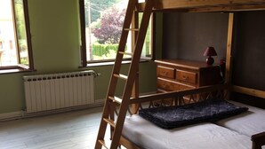 Una cama litera con escalera de madera, un aparador y una ventana con vistas a zonas verdes.