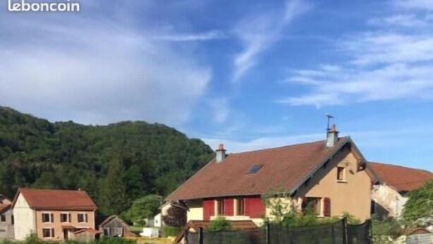 Un trampolín en un área con césped y una casa al fondo.