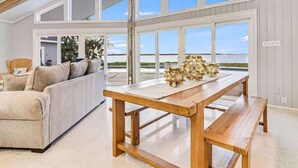 A spacious room with a high ceiling, large windows, a wooden dining table, and a beige sofa. - Whispering Breezes at Windy Hill (Ingleside)