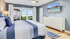 A bedroom with a bed, a dresser, a television, and a view of a swimming pool. - Whispering Breezes at Windy Hill (Ingleside)
