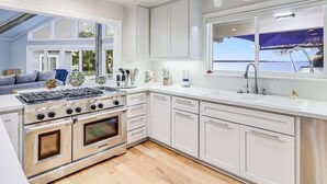 A modern kitchen with white cabinetry, a gas stove, and a large window. - Whispering Breezes at Windy Hill (Ingleside)