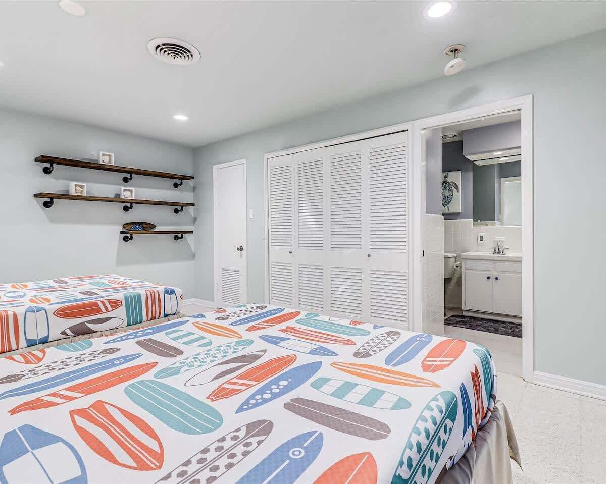 Een slaapkamer met twee bedden, een kledingkast met schuifdeuren, een badkamer met wastafel en spiegel, en planken met fotokaders.
