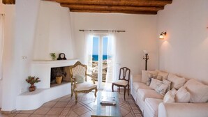 A living room with a fireplace, a sofa, a coffee table, and a view of the sea through a glass door. - Mykonian Luxury Villa Victoria with Pool (Mykonos)