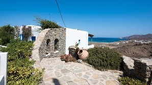 A stone pathway leading to a white building with a stone archway, surrounded by greenery and overlooking a coastal landscape. - Mykonian Luxury Villa Victoria with Pool (Mykonos)