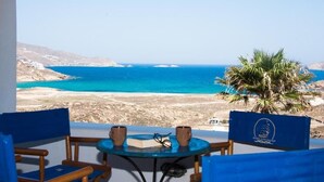A balcony with a view of the sea, a palm tree, and a table with two cups and a book. - Mykonian Luxury Villa Victoria with Pool (Mykonos)
