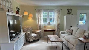 A living room with a television, armchair, sofa, coffee table, and a window with curtains. - Sunny at 135 is a wonderful place to  (Aiken)
