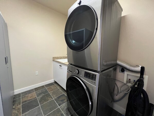 Une buanderie équipée d’une machine à laver et d’un sèche-linge superposés, d’un plan de travail avec un évier et d’un tuyau d’aération.