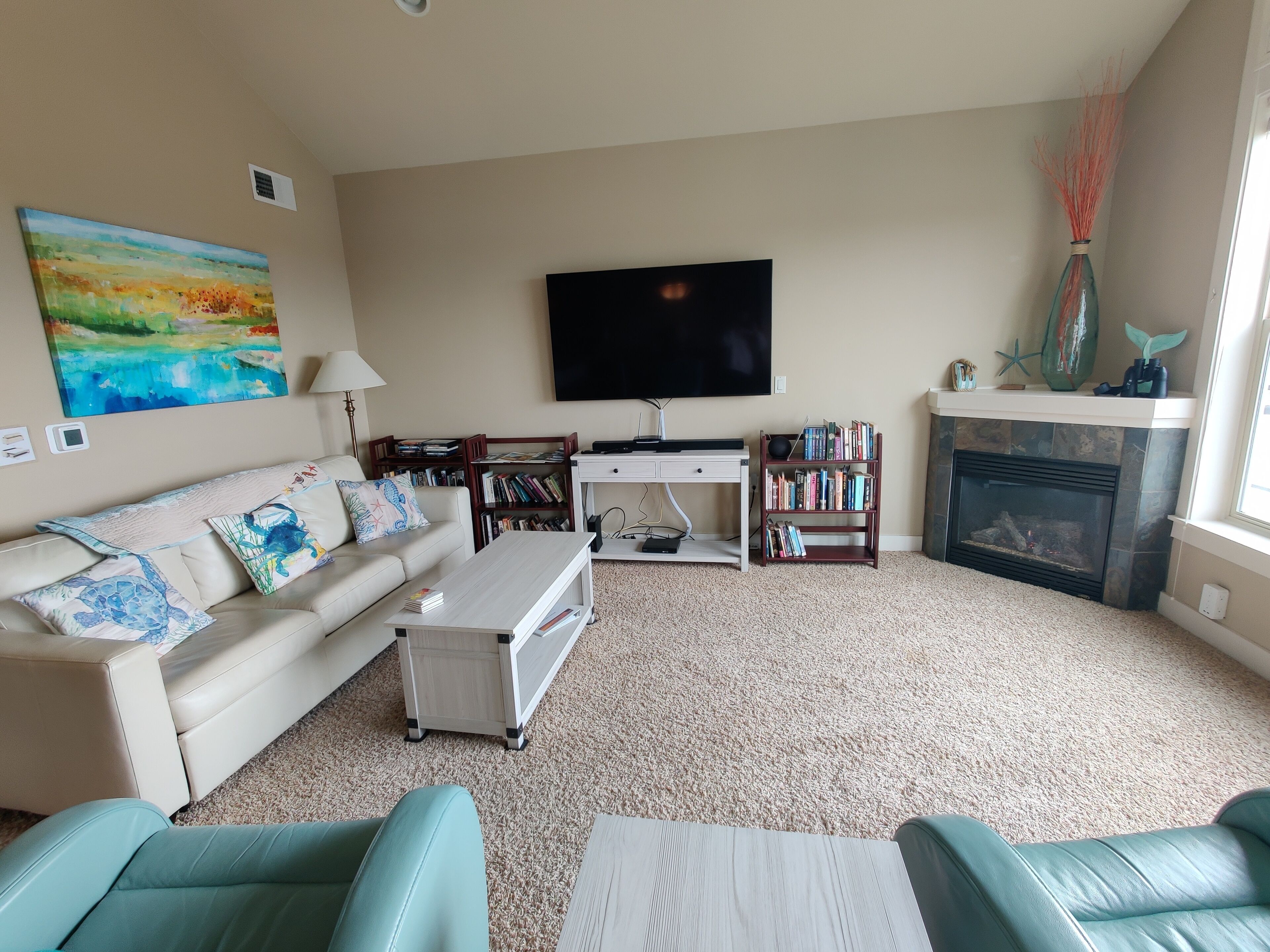 A living room with a sofa, coffee table, TV, bookshelf, fireplace, and a painting on the wall.