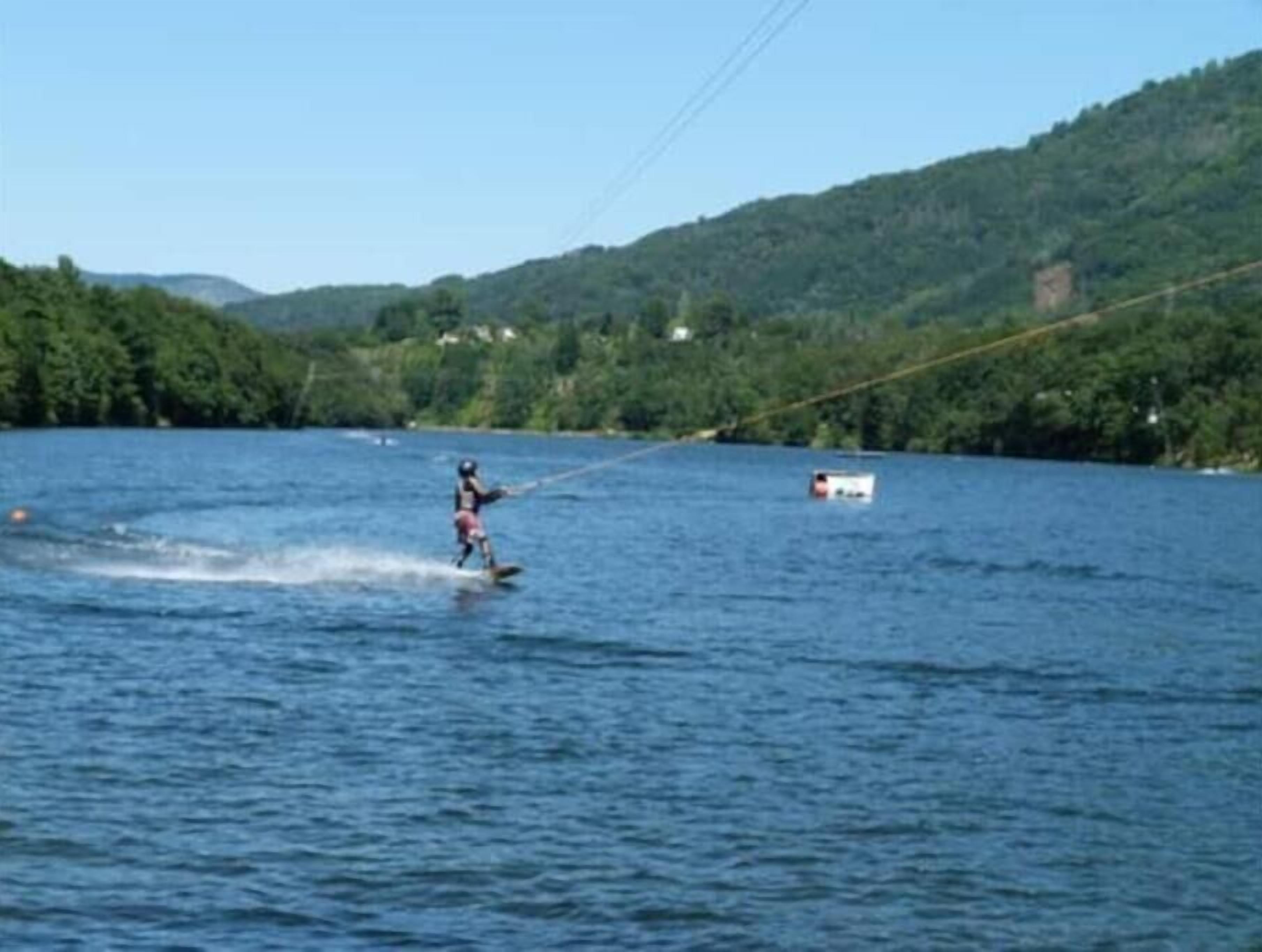 Iemand waterskieden op een meer, met een boot op de achtergrond.
