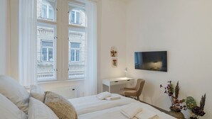 Habitación de hotel con dos camas, un escritorio, una silla, un televisor y ventana con vistas a edificios.