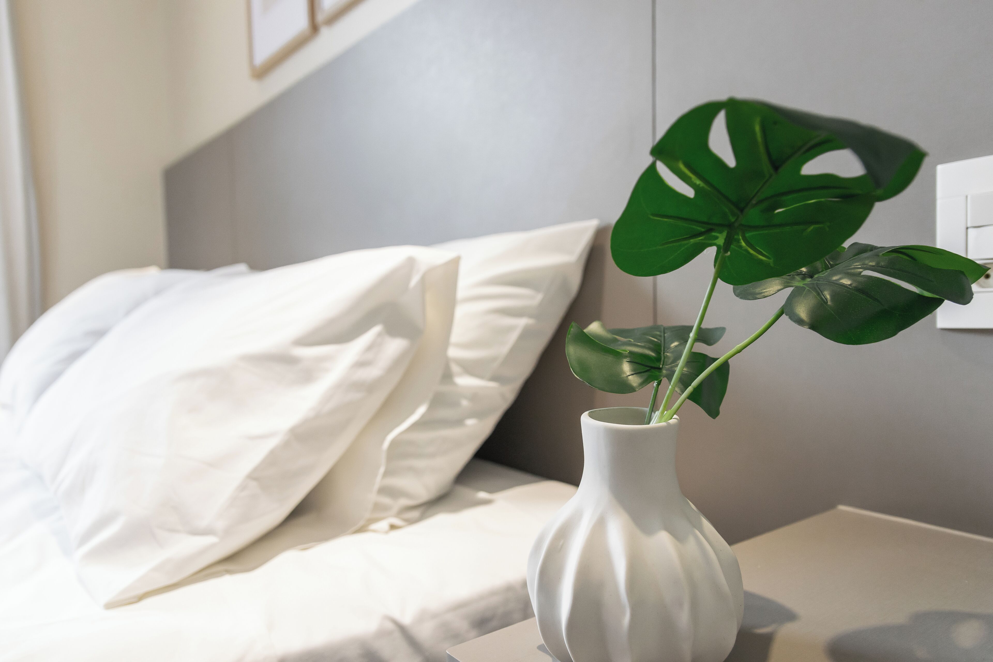 A white bedside table with a white vase containing a plant with large green leaves.