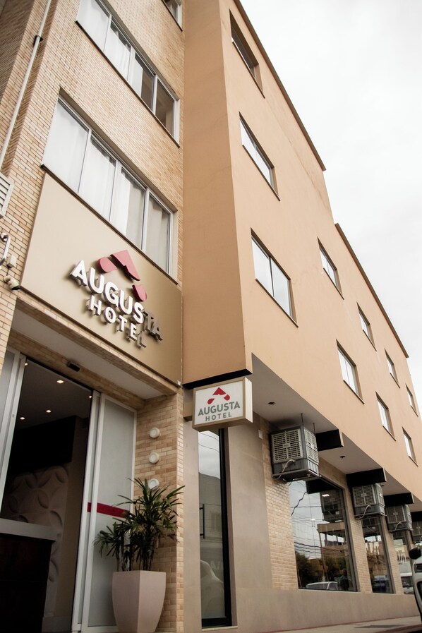 The exterior of the Augusta Hotel with a modern design, featuring a prominent sign, large windows, and a potted plant near the entrance. - Augusta Hotel by Samba (Joao Neiva)