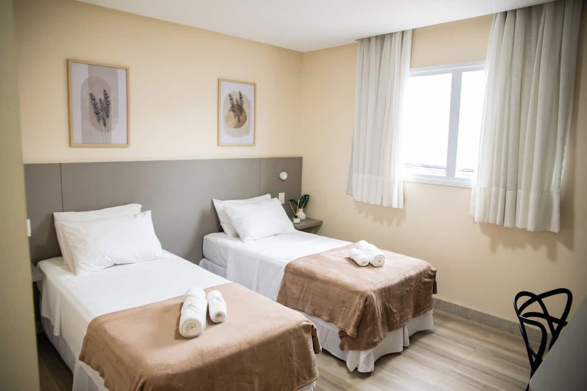 Une chambre d’hôtel avec deux lits, des murs de couleur beige et une fenêtre avec des rideaux.