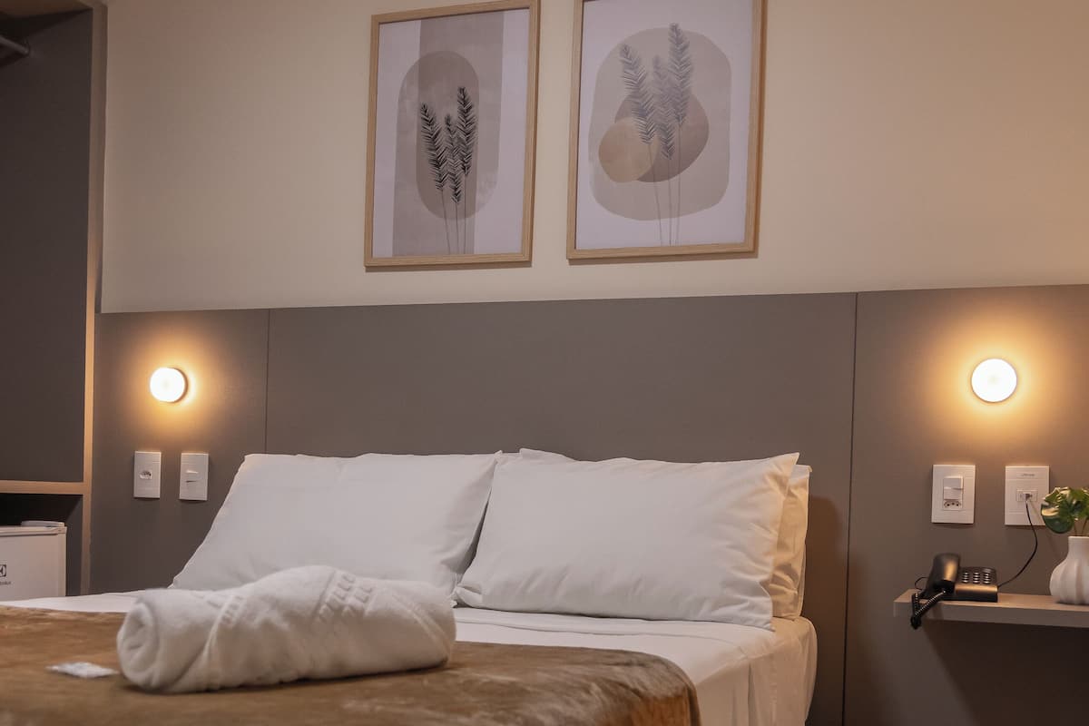 Une chambre d’hôtel moderne avec un grand lit, deux appliques murales et des œuvres d’art encadrées au-dessus du lit.