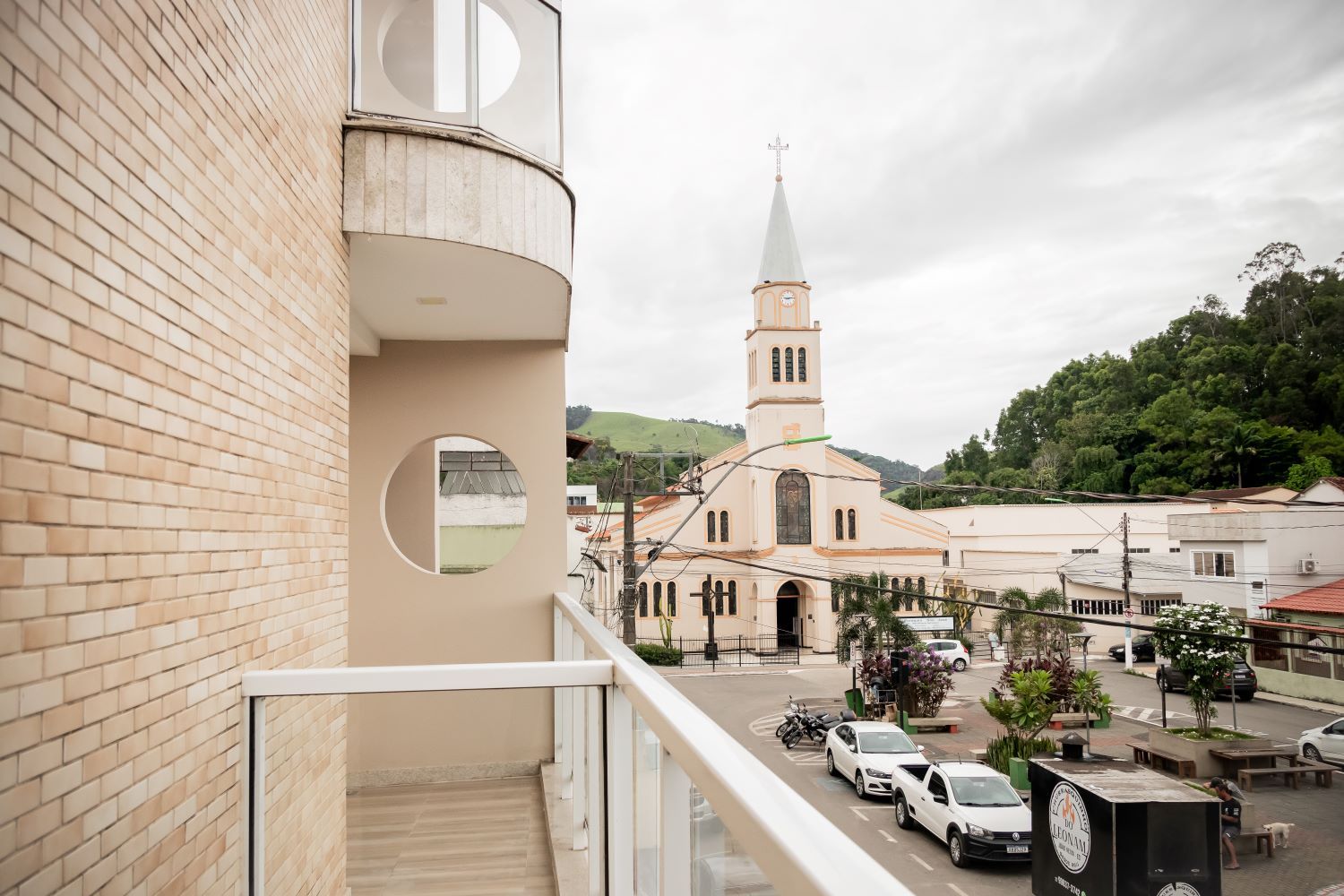 A balcony with a view of a church and a street with parked cars.