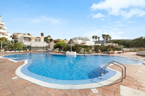A swimming pool with a tiled edge, a small island, and lounge chairs.