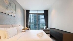 Een moderne hotelkamer met een groot bed, een nachtkastje met een lamp, een stoel en een groot raam met uitzicht op de stad.