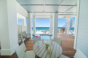 Un espace extérieur abrité, doté d’une terrasse en bois, de sièges et offrant une vue sur la plage.