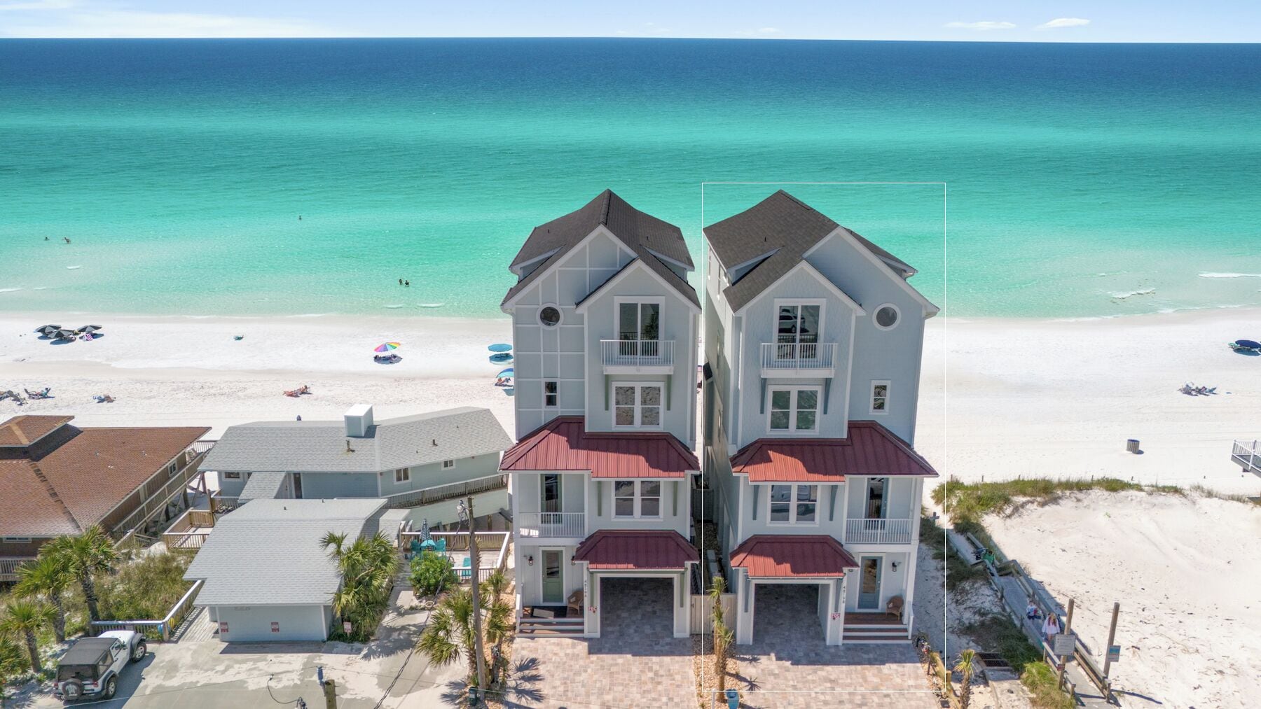 A beachfront property with a two-story house featuring a red roof, a balcony, and a garage.