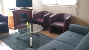 A living room with a glass coffee table, two leather armchairs, a sofa, and a television on a wooden cabinet. - Loue Maison Individuelle (Bénodet)