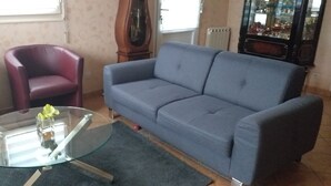 A living room with a blue sofa, two red armchairs, and a glass coffee table with a vase of flowers. - Loue Maison Individuelle (Bénodet)