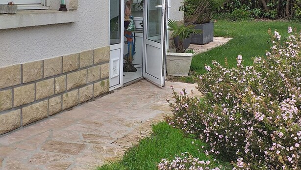 A house with a glass door leading to a covered patio area. - Loue Maison Individuelle (Bénodet)