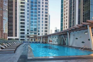 Una piscina con sillas de descanso, rodeada de edificios altos.