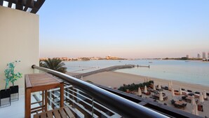 A balcony with a view of a beach, a palm tree, and a cityscape in the background. - Seaside Studio in PalmJumeirah,Beach Access (Dubai)