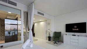 A modern hotel room with a large window, a green armchair, a flat-screen TV, and a potted orchid. - Seaside Studio in PalmJumeirah,Beach Access (Dubai)