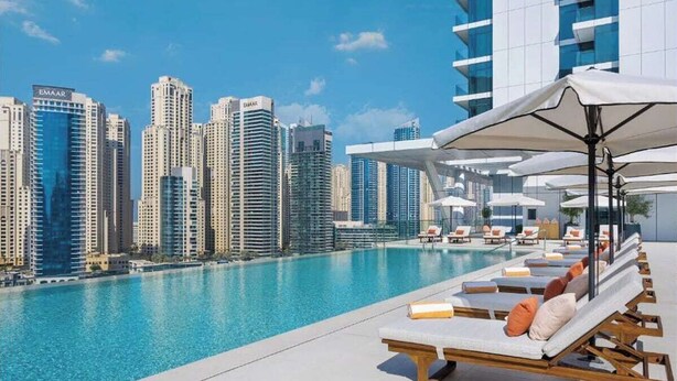 Una piscina en la azotea con sillas de descanso y sombrillas, con vistas a un paisaje urbano de edificios altos.