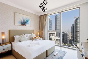 A modern hotel room with a large bed, a city view, a painting on the wall, and a nightstand with a lamp.