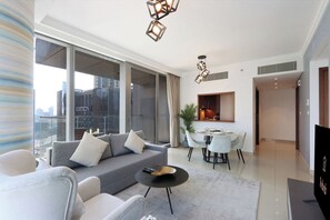 A modern living room with a sofa, dining table, and chairs, large windows, and a city view.