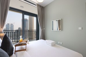 Une chambre d’hôtel avec un grand lit, une table de chevet sur laquelle se trouve un plateau de petit-déjeuner, un miroir au mur et une vue sur les bâtiments de la ville par une grande fenêtre.