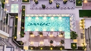 A pool area with the name 'DAMAC' prominently displayed, surrounded by outdoor seating and greenery. - Canalfront Gem 1BR in Zada Tower by Livbnb (Dubai)