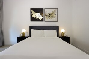 A bed with white bedding, two bedside tables with lamps, and two wall-mounted artworks depicting wings.