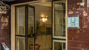 A hotel entrance with a glass door, a potted plant inside, and a checkered floor pattern. - Colonna Classic Style Apartment by Wonderful Italy (Naples)