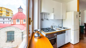 A modern kitchen with white cabinets, a gas stove, and a dishwasher. A window reveals a red-domed building outside. - Colonna Classic Style Apartment by Wonderful Italy (Naples)