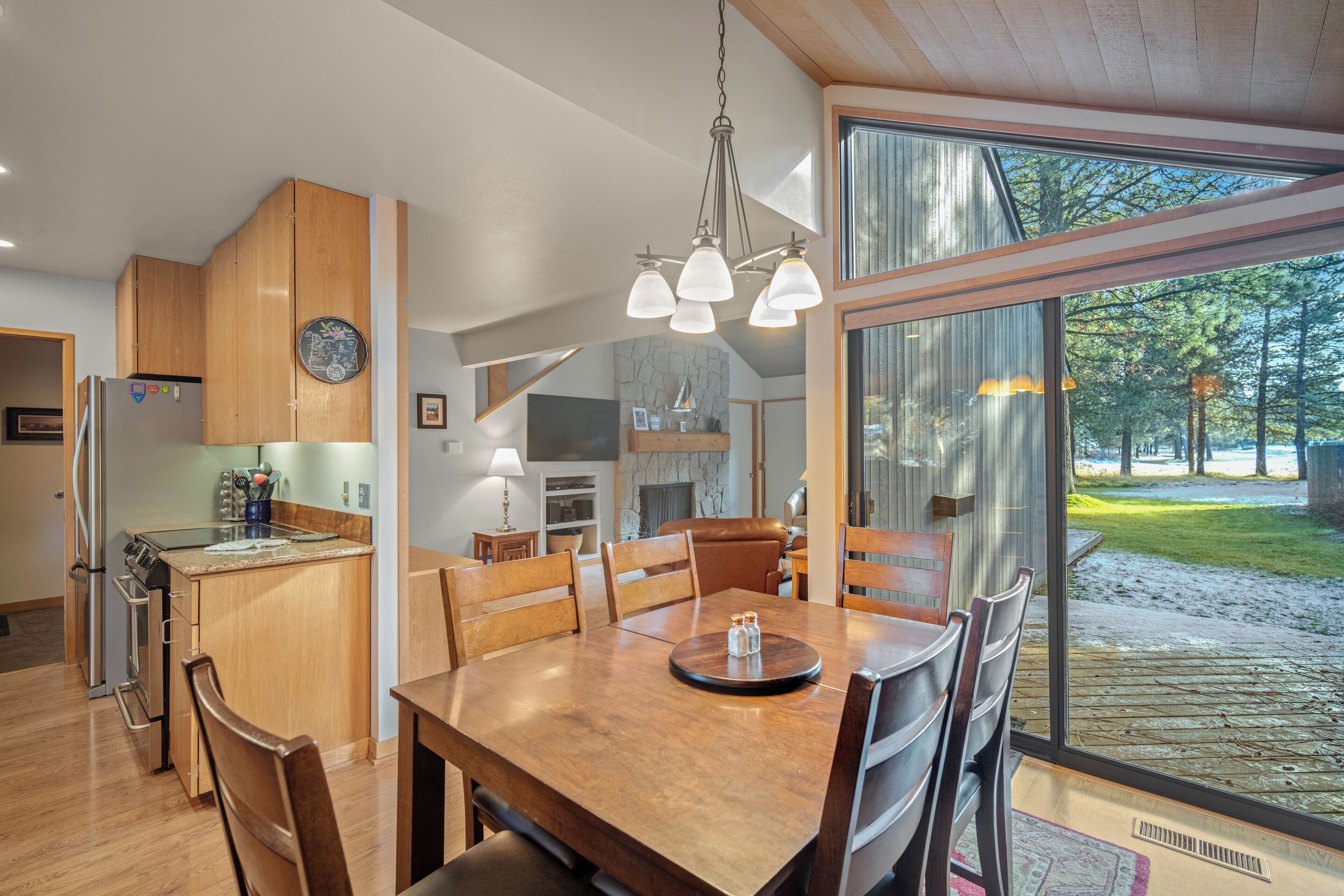 A modern kitchen with wooden cabinets, a dining table with chairs, and a large window offering a view of the outdoors.